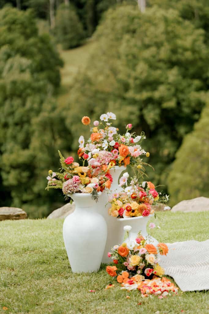 Three white urns in different sizes plus a floor arrangement decorate the Ceremony space at an outdoor wedding