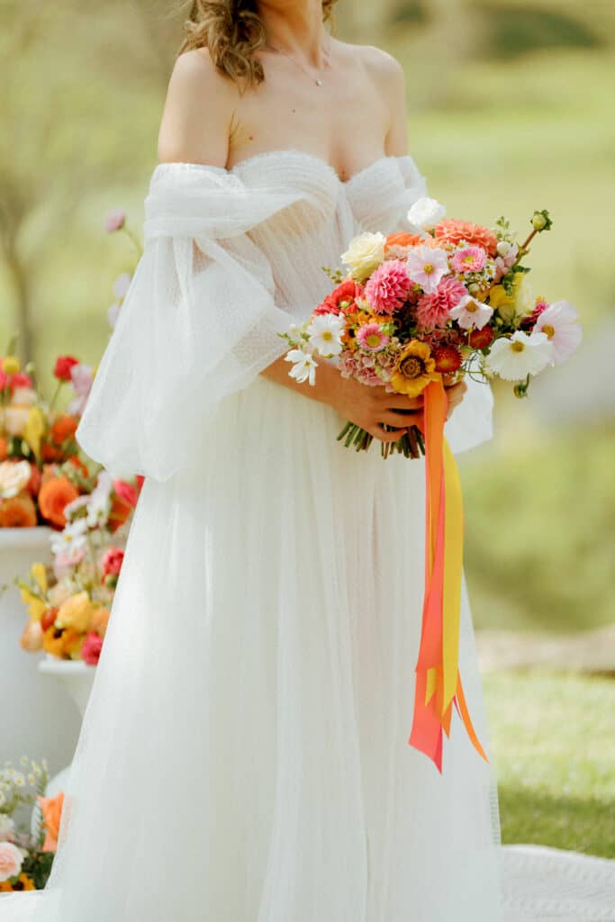 Bride at the Ceremony altar is holding bright bridal bouquet in pink, orange, yellow, white, salmon and coral colours